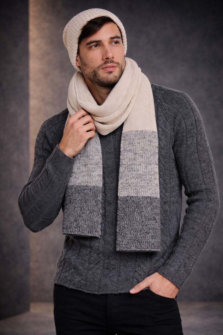 Man wearing a gray sweater and beige scarf against a dark background